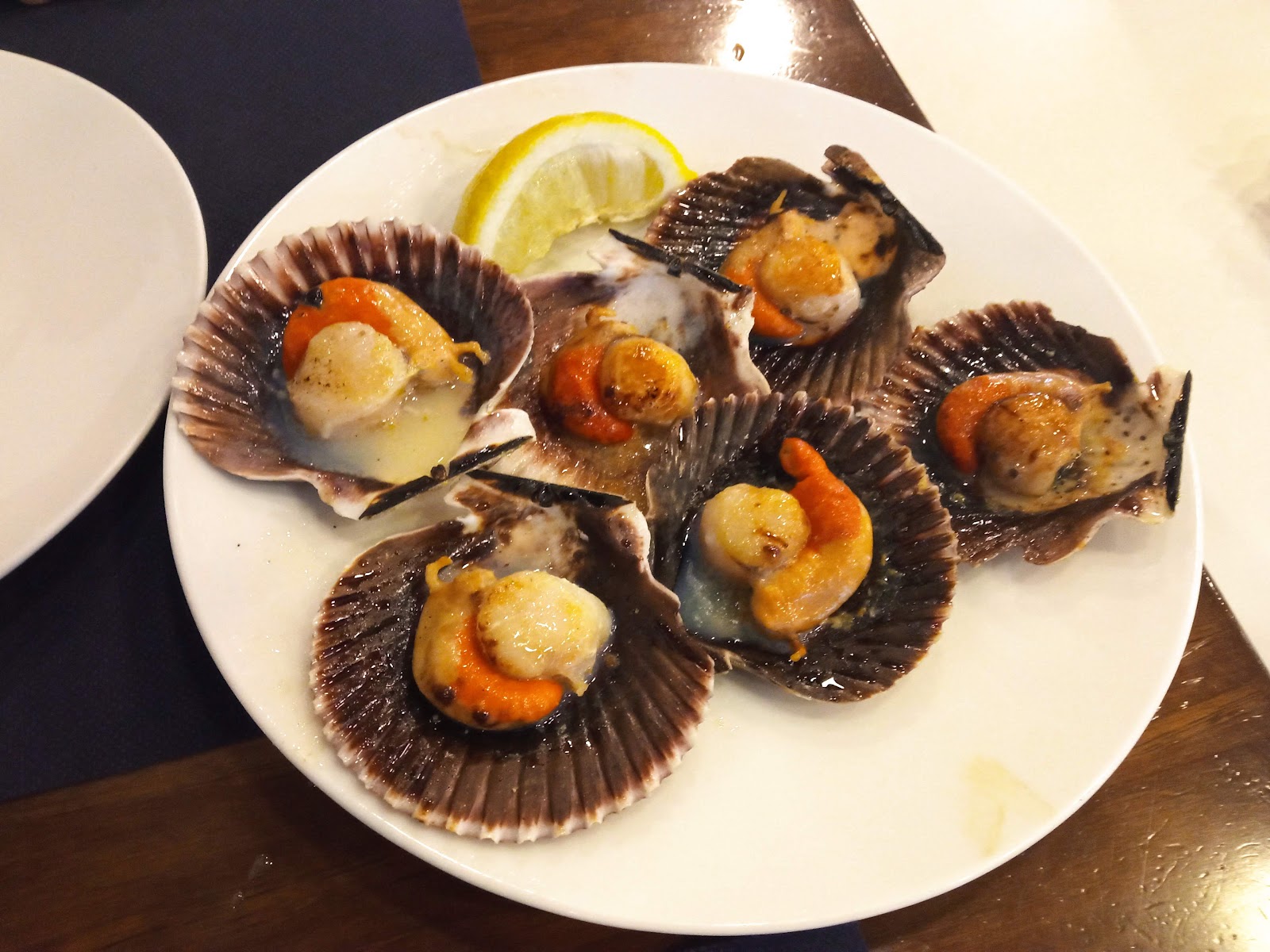 Five scallops on the half shell with bright orange roe and lemon wedge